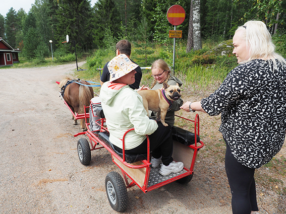 Ponirattailla kaksi kehitysvammaisten leiripäiville osallistunutta nuorta naista, joilla on sylissään koira...