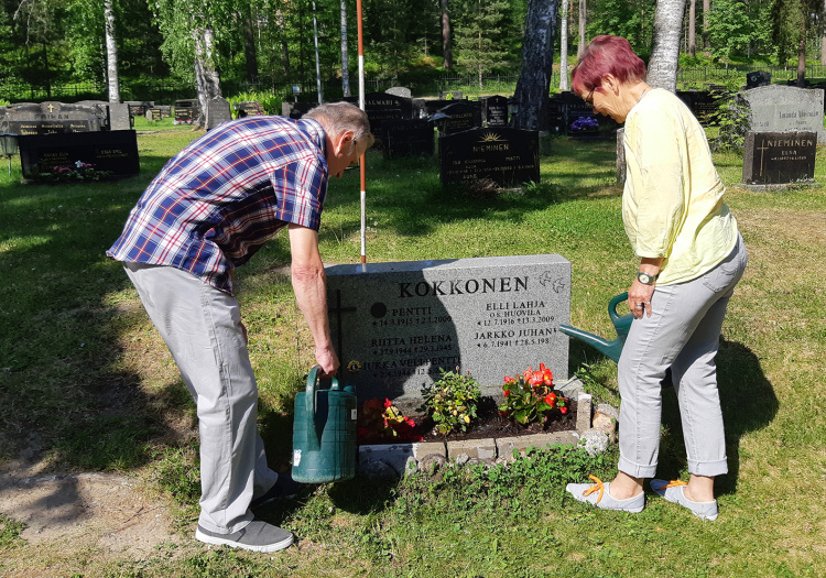 Hautausmaapäivä ja hartaushetki Mies ja nainen kastelevat haudalla olevia kukkia.