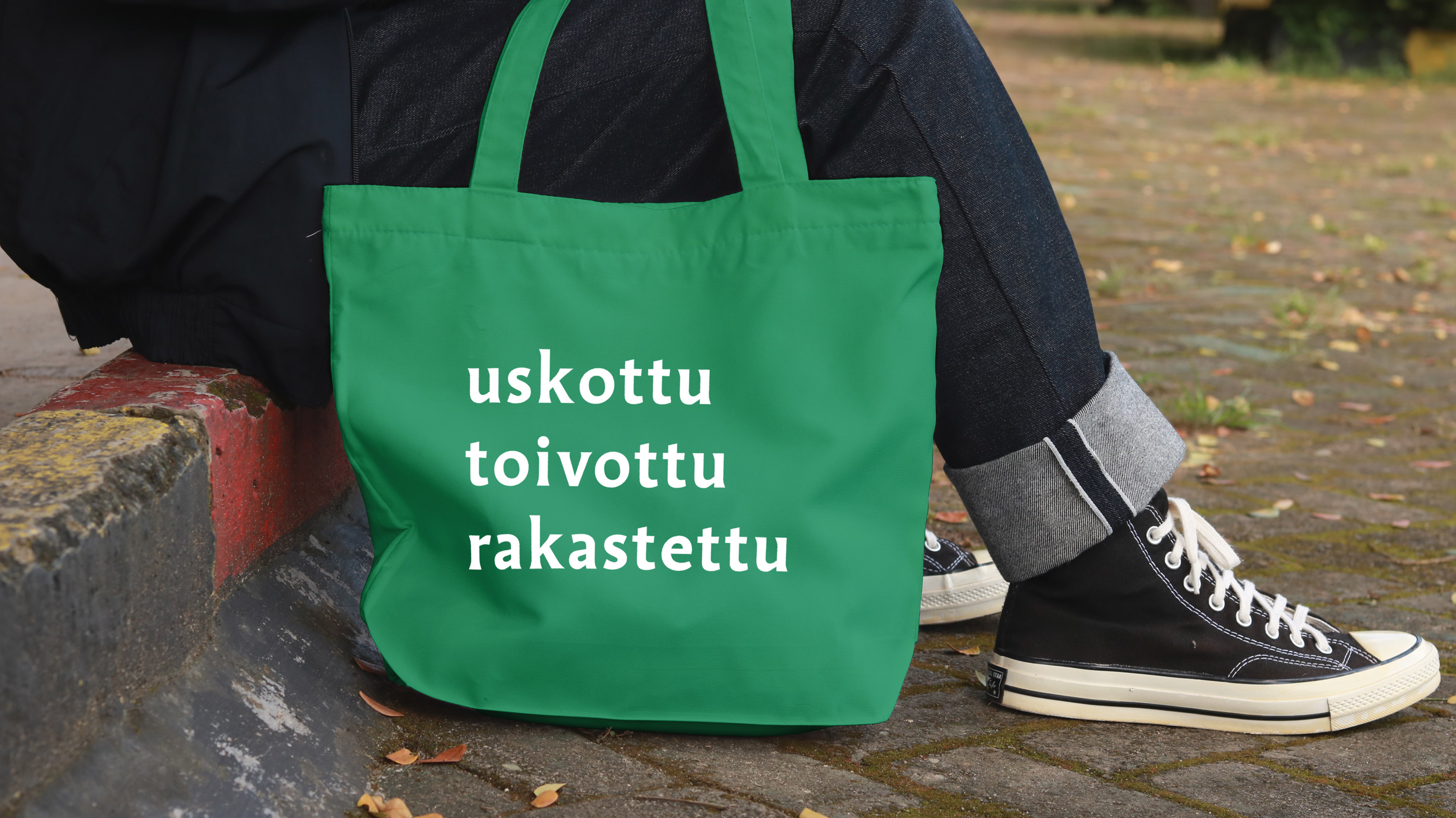 Etualalla vihreä kangaskassi, jossa teksti uskottu, toivottu rakastettu.