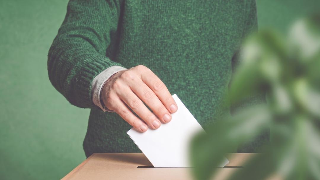 Piirroskuva, jossa käsi laittaa vaalilipukkeen uurnaan.